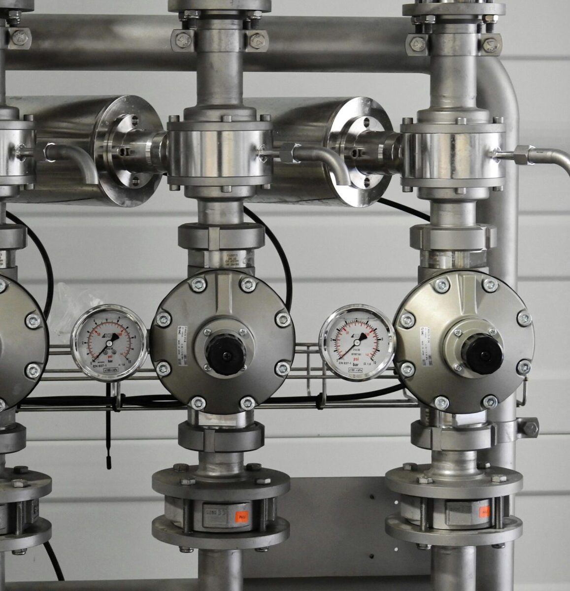 Close-up of stainless steel pipes with pressure gauges in an industrial setting.
